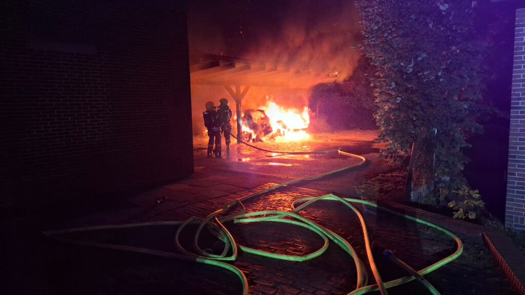 Löscharbeiten an einem brennenden Carport bei Nacht, im Vordergrund liegen Schläuche