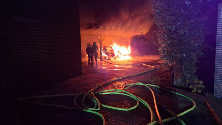 Löscharbeiten an einem brennenden Carport bei Nacht, im Vordergrund liegen Schläuche