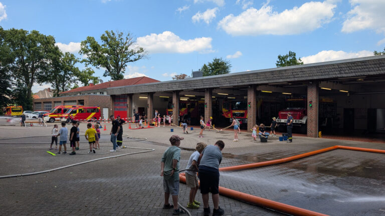Kinder spielen beim Ferienspaß mit Schläuchen und Wasser vor dem Feuerwehrhaus Hude